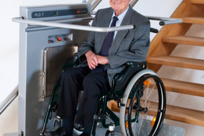 Oudere man zittend in een rolstoel op een rolstoellift die via de trap omhoog gaat