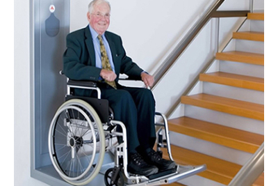 Afbeelding van een oudere man in een rolstoel die op een rolstoellift staat die onderaan de trap staat